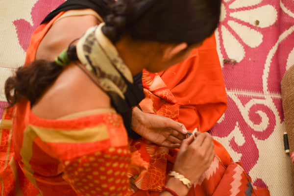 Woman hand sewing fabric in orange kurta at Sewing New Futures NGO training center's social enterprise